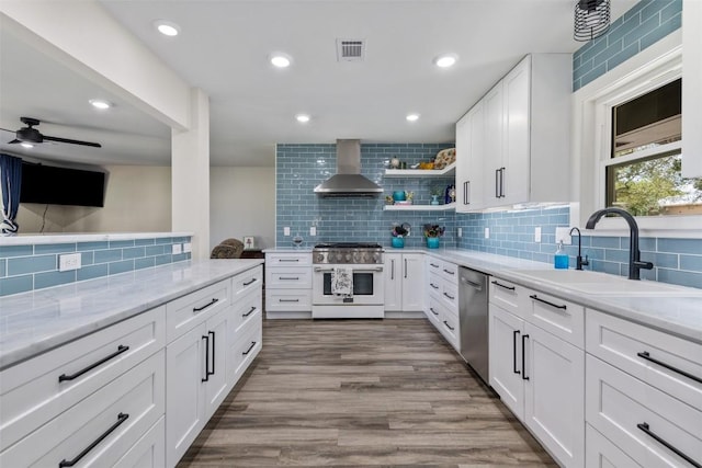 kitchen with wall chimney exhaust hood, appliances with stainless steel finishes, wood finished floors, open shelves, and a sink