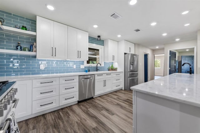 kitchen with stainless steel appliances, a sink, light stone countertops, open shelves, and dark wood finished floors