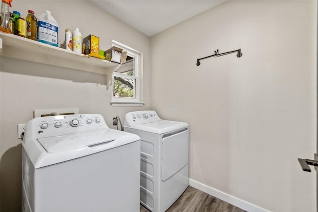 clothes washing area featuring laundry area, wood finished floors, washing machine and clothes dryer, and baseboards