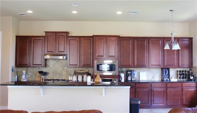 kitchen featuring dark countertops, stainless steel microwave, under cabinet range hood, and dark brown cabinets