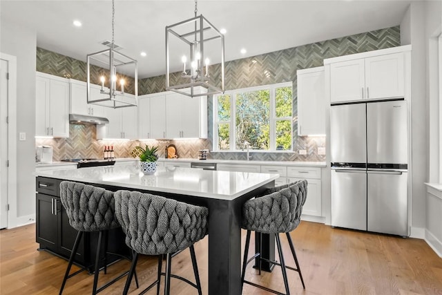 kitchen with stainless steel appliances, light countertops, white cabinets, a kitchen island, and under cabinet range hood