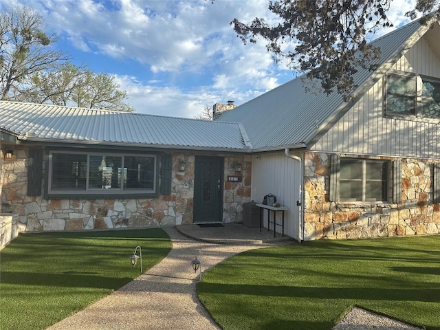 view of front of home with metal roof, stone siding, a chimney, and a front yard