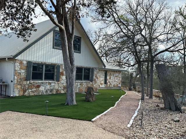 back of property with stone siding and a lawn