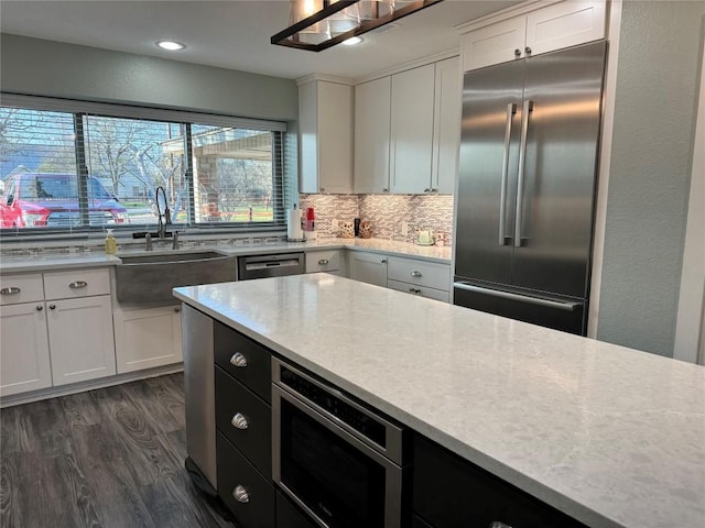 kitchen featuring dark wood-style floors, backsplash, white cabinets, a sink, and built in appliances