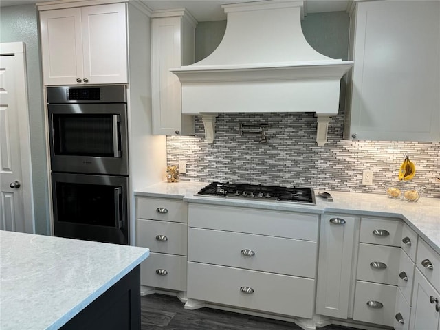 kitchen featuring dark wood-style floors, custom range hood, decorative backsplash, appliances with stainless steel finishes, and white cabinetry