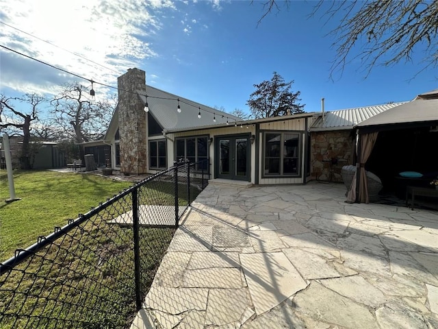 rear view of property with a chimney, a lawn, a patio area, fence, and stone siding