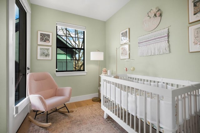 bedroom featuring a crib, baseboards, and wood finished floors