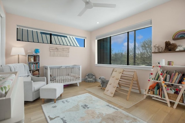 bedroom featuring a nursery area, multiple windows, baseboards, and wood finished floors