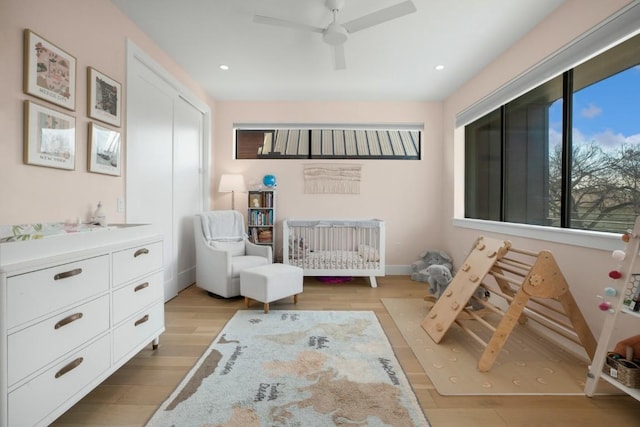 bedroom featuring recessed lighting, baseboards, light wood-style floors, a closet, and a crib