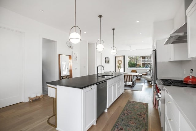 kitchen with appliances with stainless steel finishes, white cabinetry, a sink, an island with sink, and wood finished floors