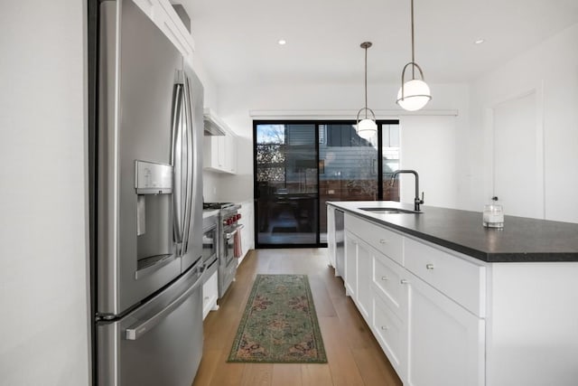 kitchen with dark countertops, appliances with stainless steel finishes, light wood-style floors, white cabinets, and a sink