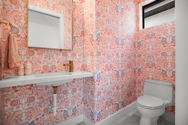 half bath featuring baseboards, toilet, and wallpapered walls