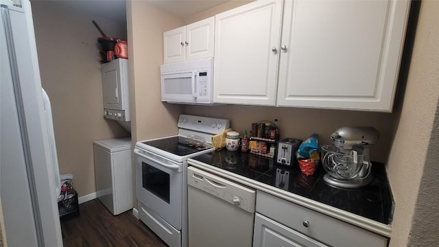 kitchen with stacked washer / drying machine, dark wood-type flooring, white cabinetry, white appliances, and baseboards