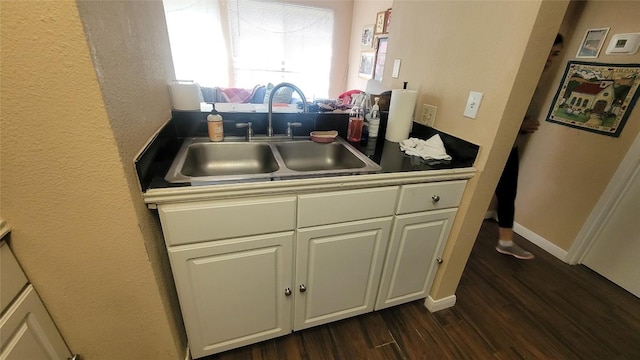 kitchen featuring dark wood-style flooring, a sink, white cabinetry, and baseboards