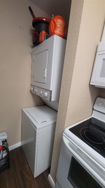 laundry room featuring laundry area, stacked washing maching and dryer, baseboards, and dark wood finished floors