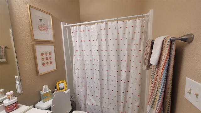 full bath with a textured wall, toilet, and a shower with curtain