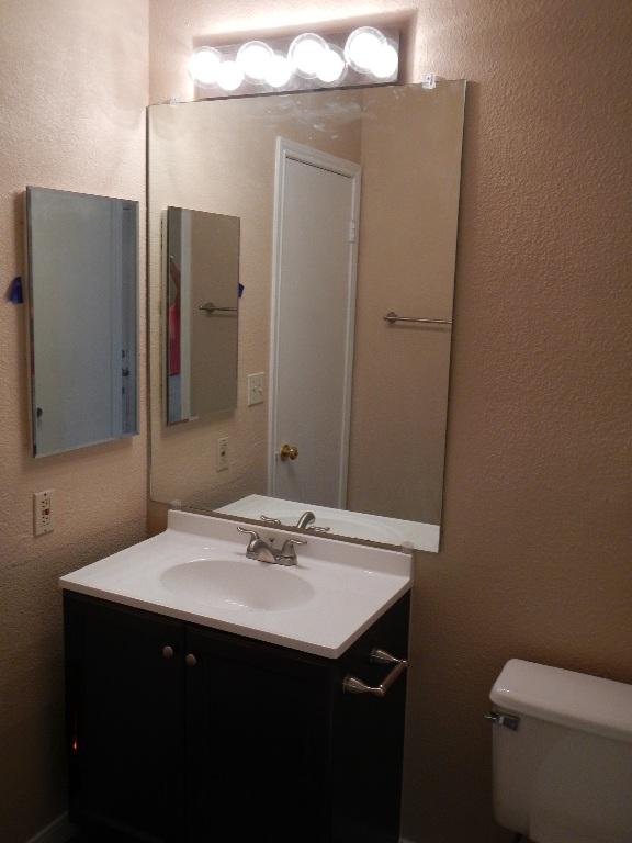 half bathroom featuring a textured wall, vanity, and toilet