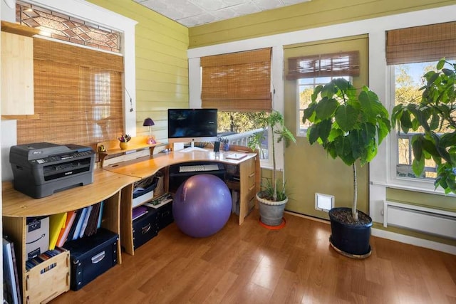 office with a baseboard heating unit, wood walls, plenty of natural light, and wood finished floors