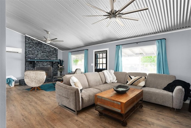 living room with ceiling fan, lofted ceiling, a stone fireplace, wood finished floors, and a wall mounted AC