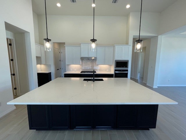 kitchen featuring oven, built in microwave, a sink, a large island, and decorative backsplash