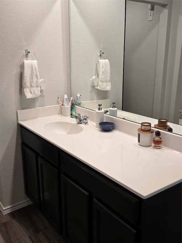 bathroom featuring a textured wall, vanity, baseboards, and wood finished floors