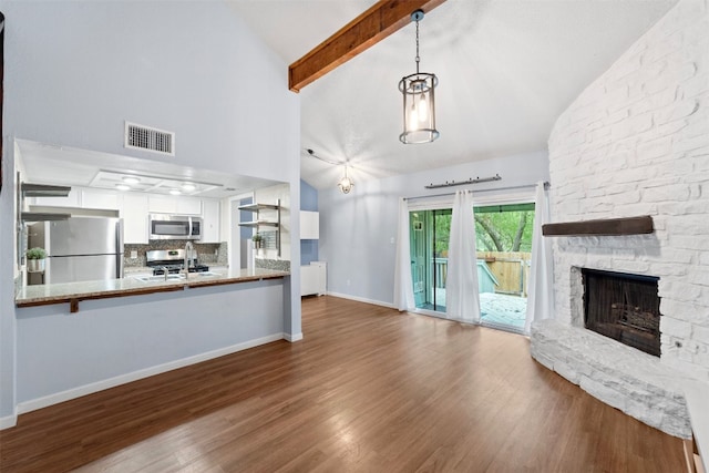 unfurnished living room with beam ceiling, a sink, a stone fireplace, wood finished floors, and baseboards