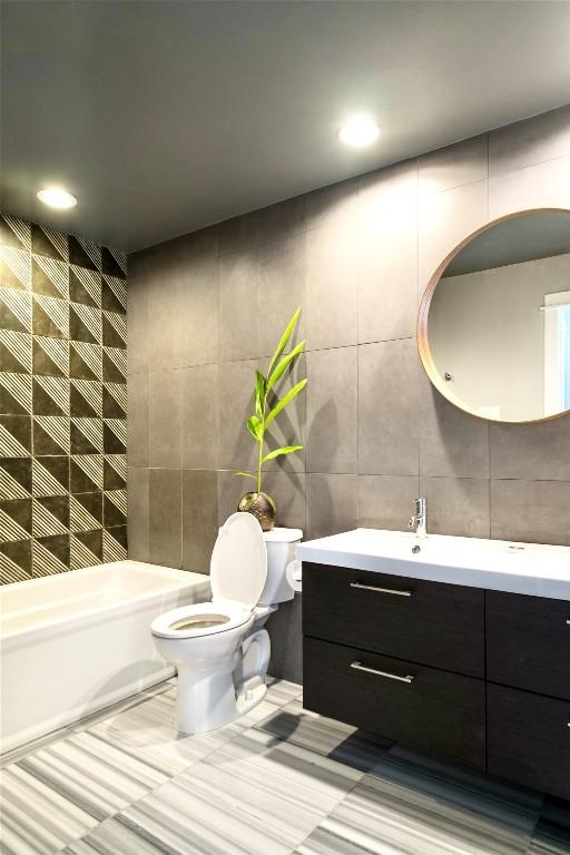 bathroom with a bathtub, toilet, tile walls, and vanity