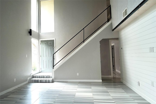 staircase featuring visible vents, wood walls, plenty of natural light, and a towering ceiling