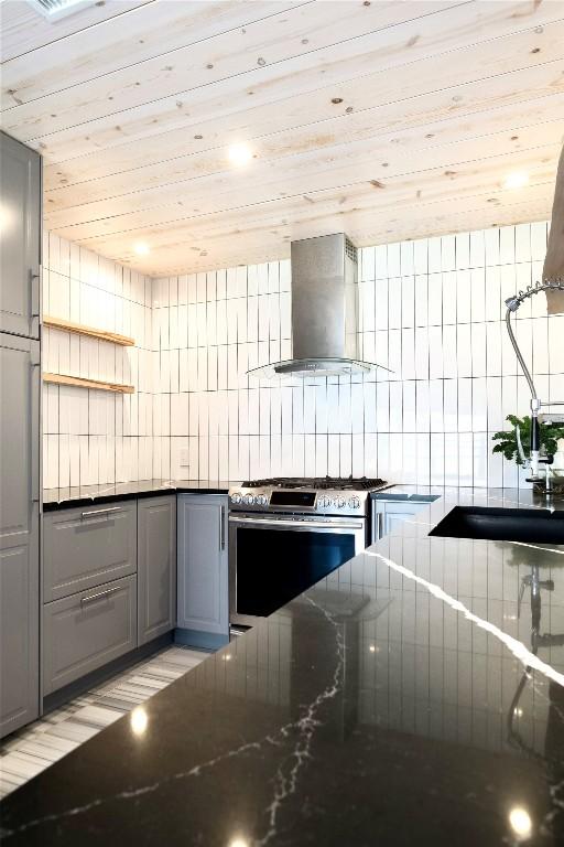 kitchen featuring wood ceiling, stainless steel range with gas cooktop, gray cabinets, and wall chimney range hood