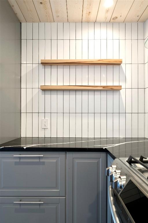 kitchen featuring open shelves, dark countertops, stainless steel range with gas stovetop, and tile walls