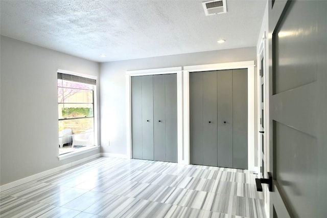 unfurnished bedroom with baseboards, a textured ceiling, visible vents, and multiple closets