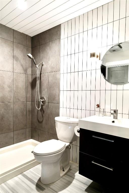 bathroom featuring a stall shower, tile walls, toilet, vanity, and backsplash