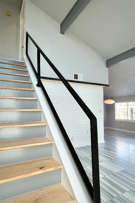 stairs featuring visible vents, lofted ceiling with beams, and baseboards