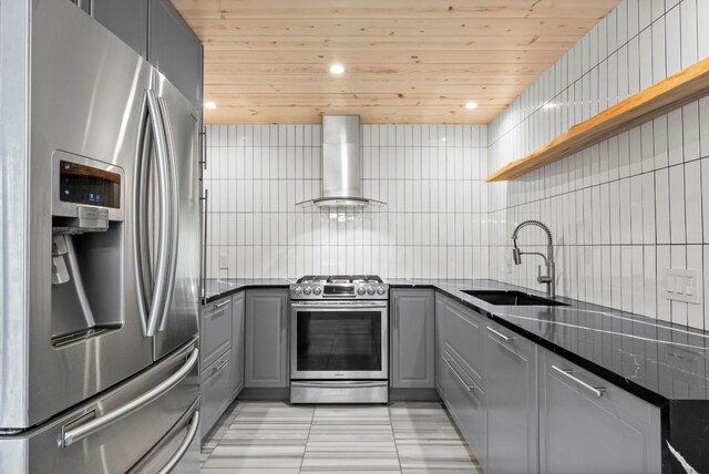 kitchen featuring stainless steel appliances, gray cabinetry, open shelves, wall chimney range hood, and a sink