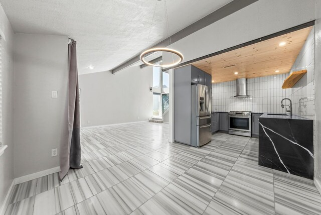 kitchen featuring wall chimney range hood, stainless steel appliances, gray cabinets, a sink, and backsplash