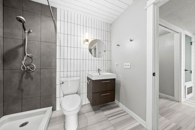 bathroom with a stall shower, vanity, tile walls, toilet, and baseboards