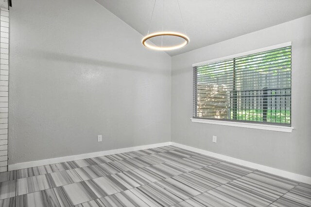 empty room featuring healthy amount of natural light, vaulted ceiling, and baseboards