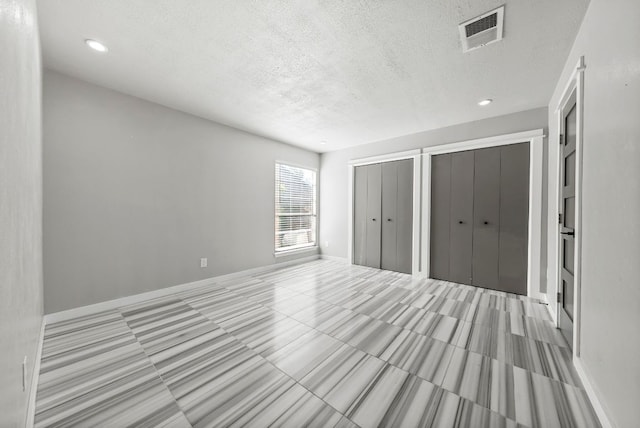 unfurnished bedroom featuring multiple closets, a textured ceiling, recessed lighting, baseboards, and tile patterned flooring