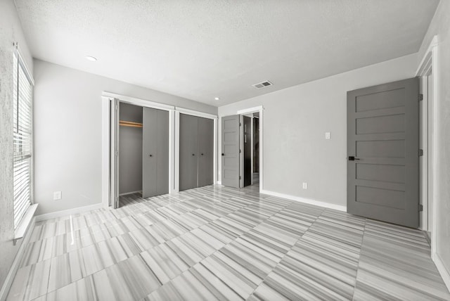 unfurnished bedroom featuring two closets, a textured ceiling, multiple windows, and baseboards