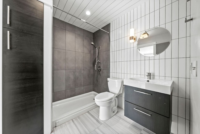 bathroom with tile walls, toilet, tiled shower, vanity, and tile patterned floors