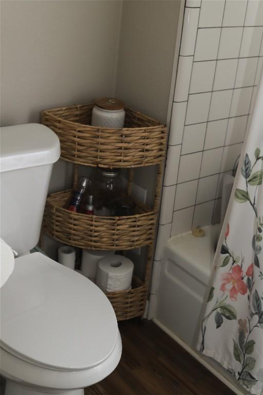 interior details featuring wood finished floors, toilet, and a shower with curtain