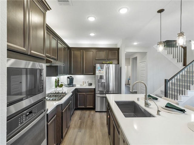 205 Bluff Creek Ln, Georgetown, TX 78628 - kitchen with appliances with stainless steel finishes, dark brown cabinetry, light countertops, light wood-type flooring, and pendant lighting