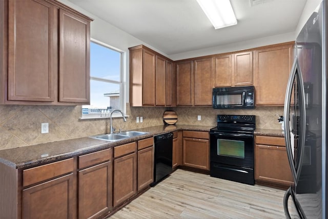 kitchen with a sink, light wood-type flooring, backsplash, black appliances, and brown cabinetry