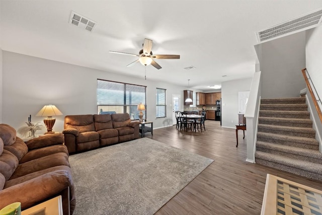 living area with ceiling fan, stairs, visible vents, and wood finished floors