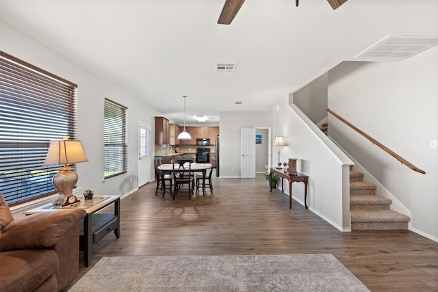 living area featuring dark wood-style floors, visible vents, and stairs