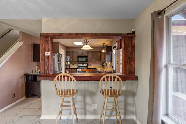 103 Ryan Cv, Hutto, TX 78634 - kitchen featuring appliances with stainless steel finishes, light tile patterned flooring, a kitchen bar, a peninsula, and hanging light fixtures