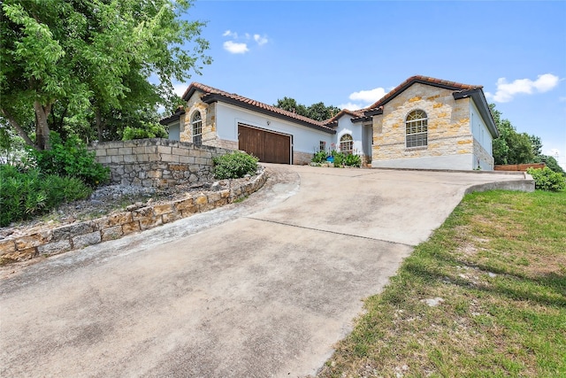 mediterranean / spanish house with stone siding, a tile roof, an attached garage, and concrete driveway