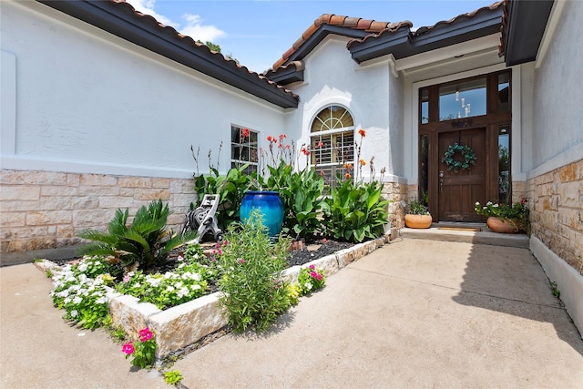 doorway to property featuring stone siding, a tiled roof, and stucco siding