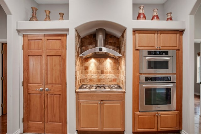 kitchen with arched walkways, light countertops, appliances with stainless steel finishes, wall chimney exhaust hood, and tasteful backsplash