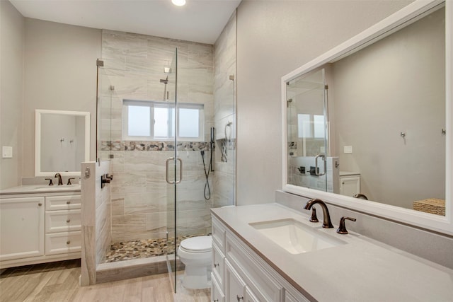 full bath featuring toilet, a shower stall, two vanities, and a sink